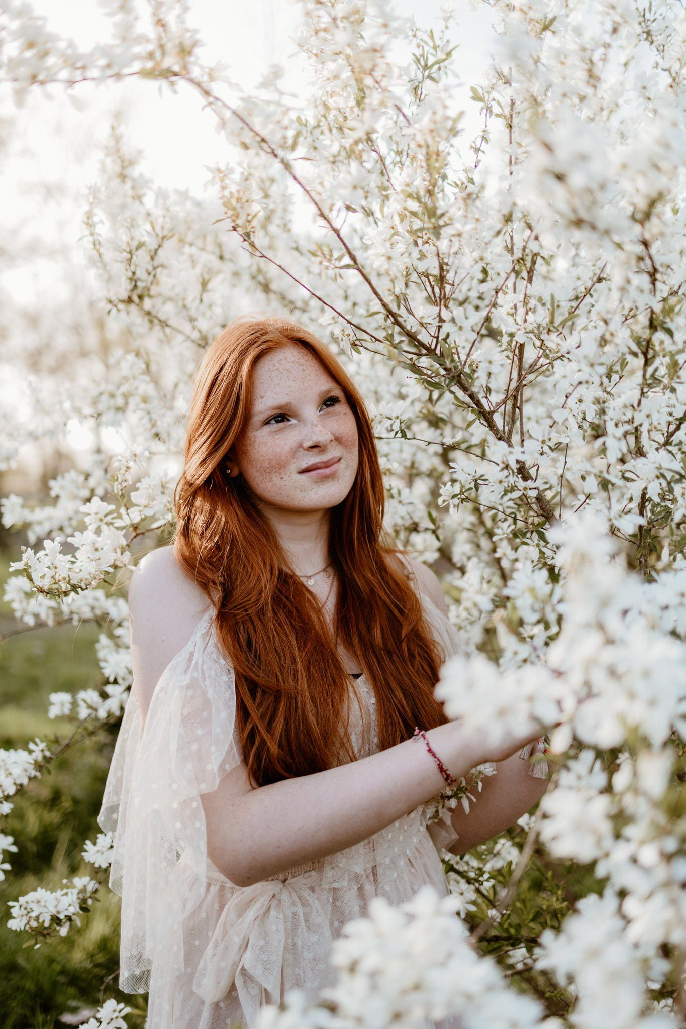 portrait d'une jeune fille aux cheveux longs roux au milieu d'un arbre aux fleurs blanches - marine delforge photographe à Pau