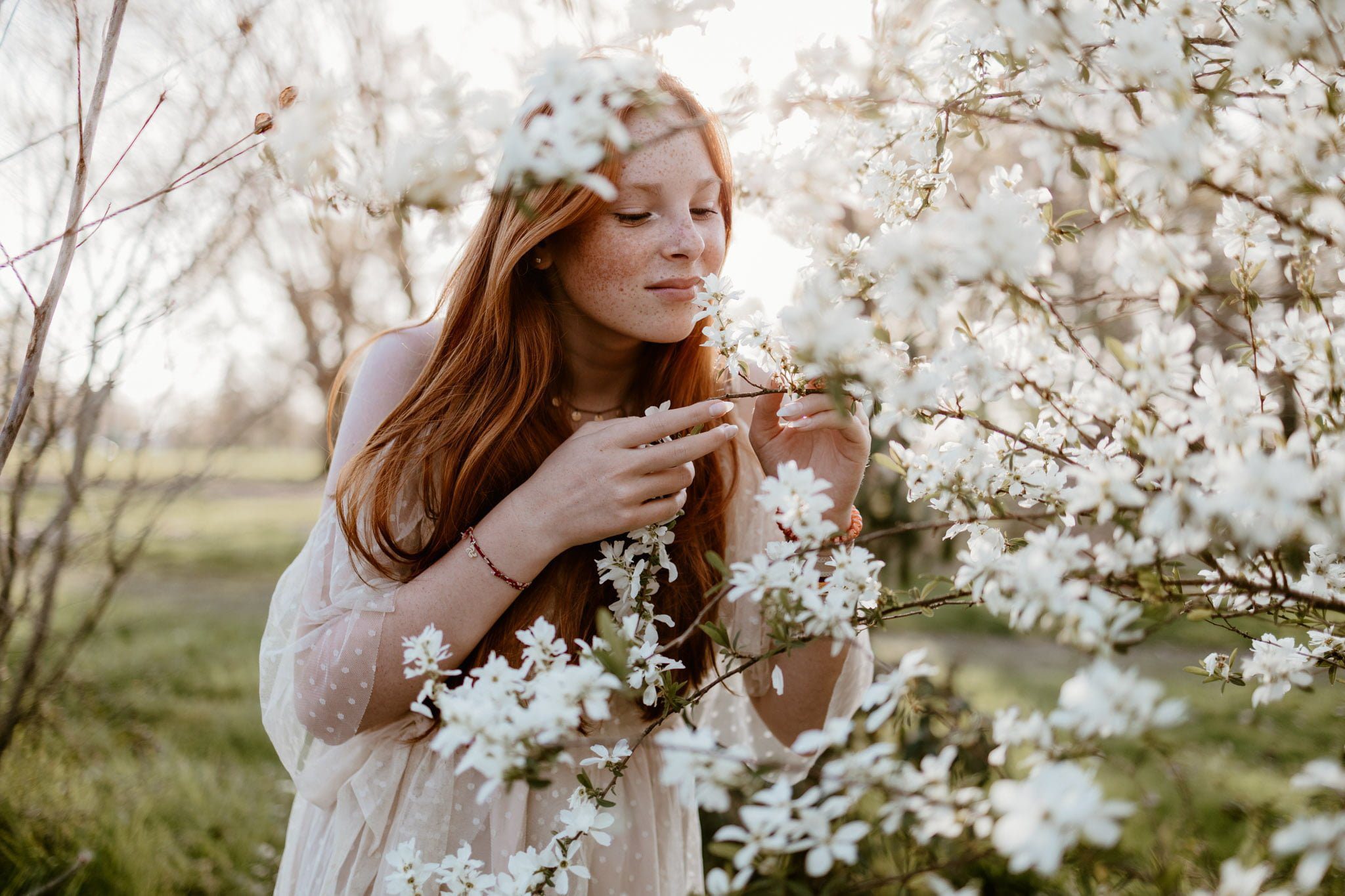 portrait d'une jeune fille aux cheveux longs roux au milieu d'un arbre aux fleurs blanches - marine delforge photographe à Pau
