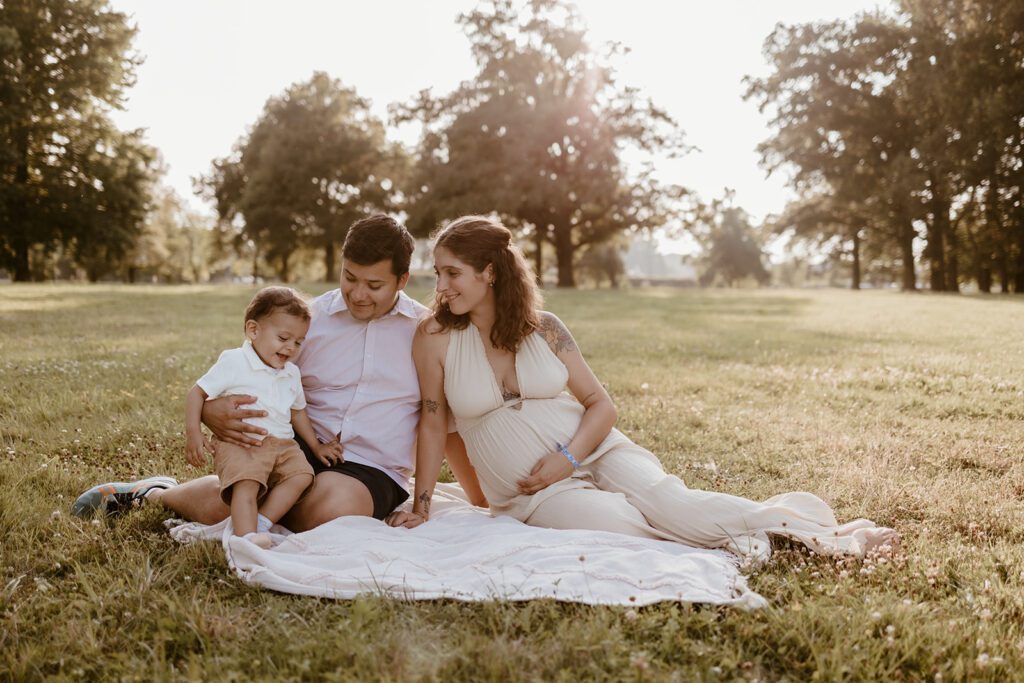 Parents qui attendent un enfant posent avec leur premier bébé au coucher du soleil. Photo par Marine Delforge photographe à Pau www.marinedelforge.fr